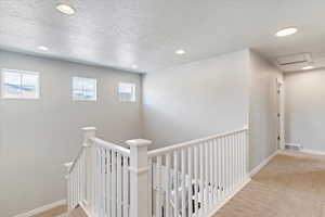 Hall with a textured ceiling, carpet flooring, recessed lighting, baseboards, and an upstairs landing