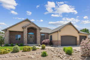 View of front facade featuring brick siding, an attached garage, stucco siding, driveway, and roof with shingles