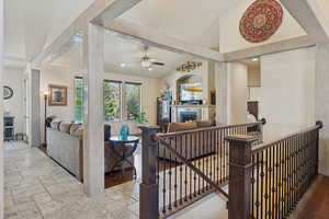 Living room featuring ceiling fan, a warm lit fireplace, stone tile flooring, recessed lighting, and vaulted ceiling