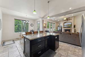 Kitchen featuring stone tile floors, dark cabinetry, recessed lighting, a ceiling fan, and a lit fireplace