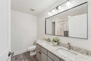 Bathroom featuring toilet, a shower stall, double vanity, baseboards, and tile patterned floors