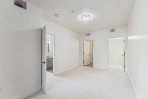 Unfurnished bedroom featuring light colored carpet, a spacious closet, baseboards, and ensuite bath
