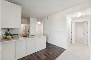 Kitchen featuring a peninsula, a sink, light stone counters, baseboards, and white cabinets