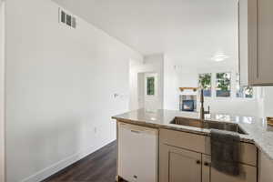 Kitchen with white dishwasher, a sink, a fireplace, light stone counters, and a peninsula