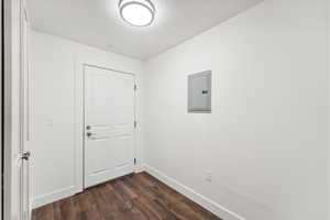 Empty room featuring electric panel, baseboards, and dark wood-type flooring