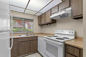 Kitchen featuring white appliances, under cabinet range hood, a sink, and light countertops