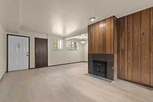 Unfurnished living room featuring baseboards, light wood-type flooring, and a tiled fireplace
