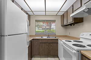Kitchen with white appliances, under cabinet range hood, a sink, and light countertops