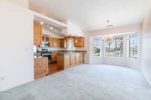 Kitchen featuring appliances with stainless steel finishes, lofted ceiling, light carpet, a chandelier, and baseboards