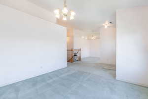 Empty room featuring a chandelier, light colored carpet, and baseboards