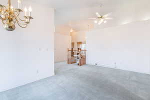 Unfurnished living room featuring light carpet, ceiling fan, vaulted ceiling, a chandelier, and baseboards