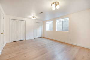 Unfurnished bedroom featuring light wood-style flooring, multiple closets, baseboards, and a textured ceiling