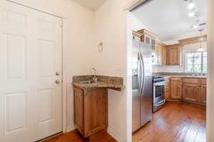 Kitchen featuring appliances with stainless steel finishes, a sink, wood-type flooring, brown cabinets, and glass insert cabinets