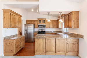 Kitchen featuring stainless steel appliances, lofted ceiling, a sink, a peninsula, and wood finished floors