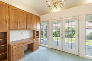 Unfurnished office with light colored carpet, vaulted ceiling, built in desk, a chandelier, and french doors