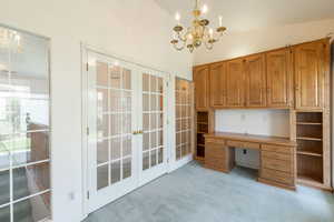 Unfurnished office with a chandelier, french doors, light carpet, built in desk, and high vaulted ceiling