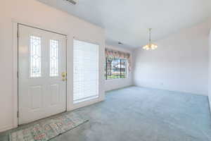 Carpeted entrance foyer with a chandelier and baseboards