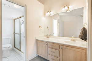 Bathroom with toilet, double vanity, a stall shower, and tile patterned flooring