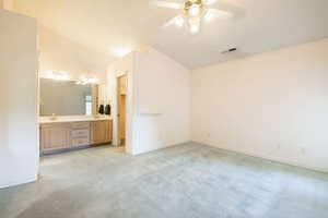 Bathroom featuring ceiling fan, vaulted ceiling, double vanity, and baseboards