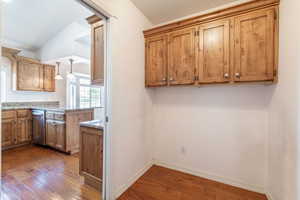 Kitchen featuring vaulted ceiling, stainless steel dishwasher, dark wood finished floors, a peninsula, and brown cabinets
