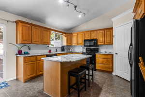 Kitchen with black appliances, vaulted ceiling, a sink, a kitchen island, and brown cabinets