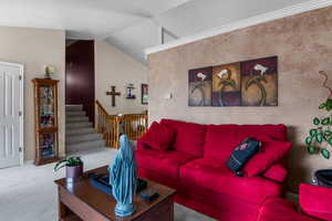 Carpeted living room featuring vaulted ceiling, stairs, and baseboards