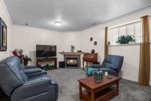 Carpeted living room with a textured ceiling, ornamental molding, a fireplace with flush hearth, and baseboards