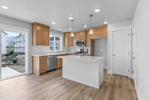 Kitchen with appliances with stainless steel finishes, light wood-style floors, brown cabinets, light countertops, and decorative light fixtures