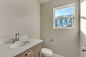 Half bathroom with vanity, toilet, and baseboards