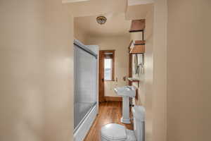 Full bathroom with wood finished floors, toilet, shower / bath combination with glass door, and baseboards