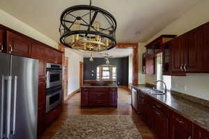 Kitchen with stainless steel appliances, a sink, dark brown cabinets, and dark wood-style flooring