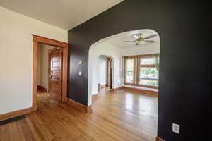 Spare room with arched walkways, ceiling fan, light wood-style flooring, and baseboards