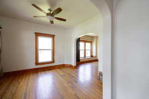 Empty room with arched walkways, wood-type flooring, baseboards, and ceiling fan