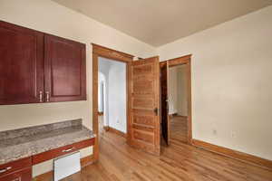 Unfurnished office featuring arched walkways, light wood-style flooring, and baseboards