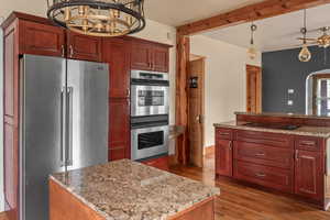 Kitchen with appliances with stainless steel finishes, light wood-style floors, a kitchen island, decorative light fixtures, and light stone countertops