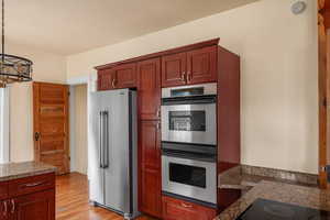 Kitchen featuring appliances with stainless steel finishes, light wood finished floors, hanging light fixtures, and dark stone counters