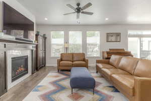 Living room with a fireplace, a ceiling fan, light wood-style flooring, recessed lighting, and baseboards
