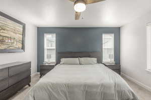 Bedroom with light carpet, multiple windows, baseboards, and a textured ceiling