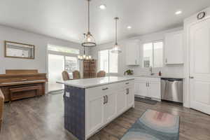 Kitchen featuring stainless steel dishwasher, a sink, a kitchen island, white cabinets, and light countertops