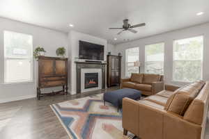 Living room featuring a ceiling fan, wood finished floors, a glass covered fireplace, baseboards, and recessed lighting