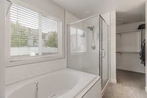 Bathroom featuring a stall shower, a bath, a spacious closet, and baseboards