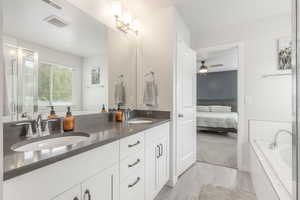 Ensuite bathroom featuring ceiling fan, tiled tub, double vanity, and a shower with shower door