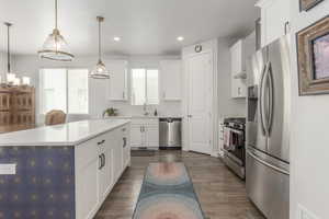 Kitchen featuring appliances with stainless steel finishes, recessed lighting, white cabinets, decorative light fixtures, and a sink