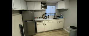 Basement unit-Kitchen featuring freestanding refrigerator, a sink, a paneled ceiling, light countertops, and white cabinetry
