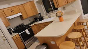 Main unit-Kitchen featuring stainless steel electric range oven, a breakfast bar area, under cabinet range hood, a sink, and light countertops