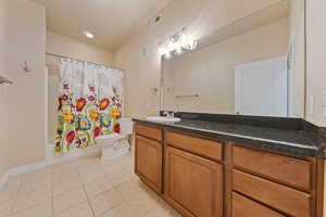 Full bathroom with toilet, tile patterned flooring, vanity, shower / bathtub combination with curtain, and baseboards