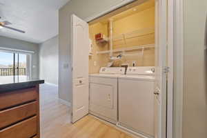 Washroom featuring independent washer and dryer, light wood-type flooring, baseboards, ceiling fan, and a textured ceiling
