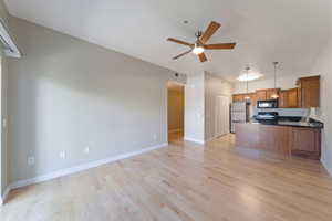 Kitchen featuring appliances with stainless steel finishes, brown cabinets, open floor plan, ceiling fan, and dark countertops