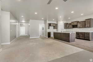 Kitchen featuring dark brown cabinetry, a sink, recessed lighting, baseboards, and a center island with sink