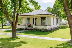 View of front of home featuring brick siding, a chimney, a porch, a front lawn, and metal roof